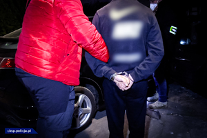 policjant pilnuje osoby zatrzymanej w trakcie przeszukania pojazdu