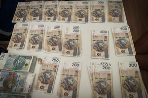 Kilkaset banknotów o nominałach 200 PLN rozłożonych na blacie stołu. Obok pliki banknotów o nominałach 100 i 500 PLN.