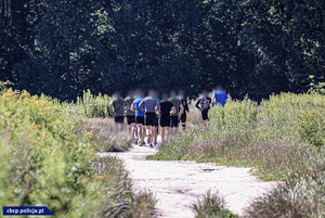 Grupa kilkunastu osób biegnąca piaszczystą ścieżką.