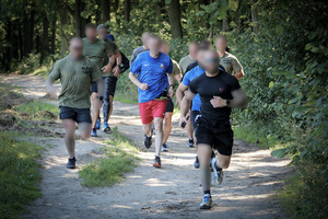 Kilkunastu policjantów w strojach do ćwiczeń biegnących w lesie.