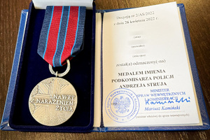 Medal w pudełku oraz legitymacja dotycząca nadania medalu, leżące na blacie stołu.