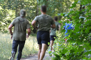 Policjanci w strojach do ćwiczeń biegnących w lesie.