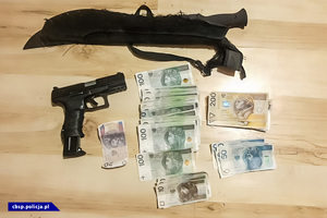Maczeta, pistolet, banknoty o nominałach 10, 20, 50, 100 oraz 200 PLN leżące na podłodze.
