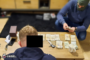 Funkcjonariusz liczący liczne banknoty o nominałach 100 i 200 PLN leżące na stole.